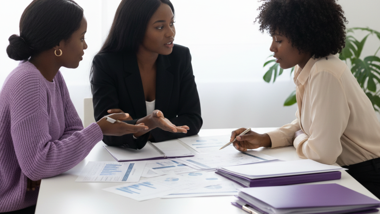 Three women discuss financial charts and documents, focusing on bookkeeping strategies in a bright office.