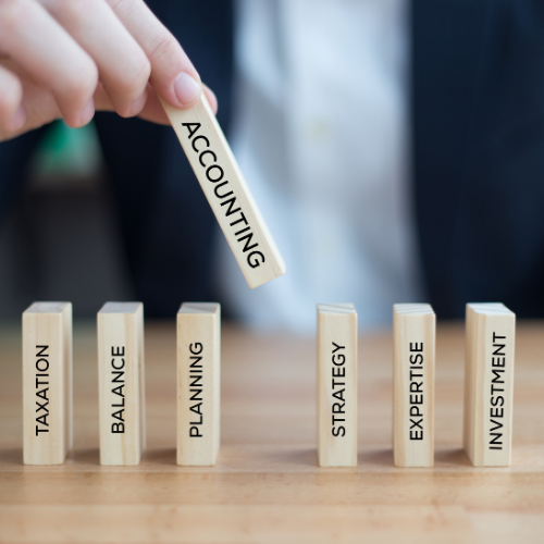A hand places a wooden block labeled ACCOUNTING among other financial blocks labeled with business terms.